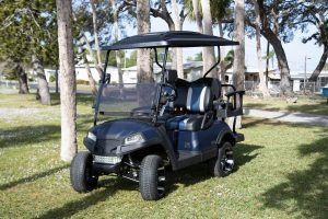 Blue golf cart parked on grass, with a black roof and seats.