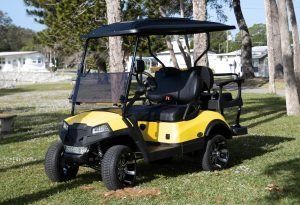Yellow and black golf cart on grass, with black roof and wheels.