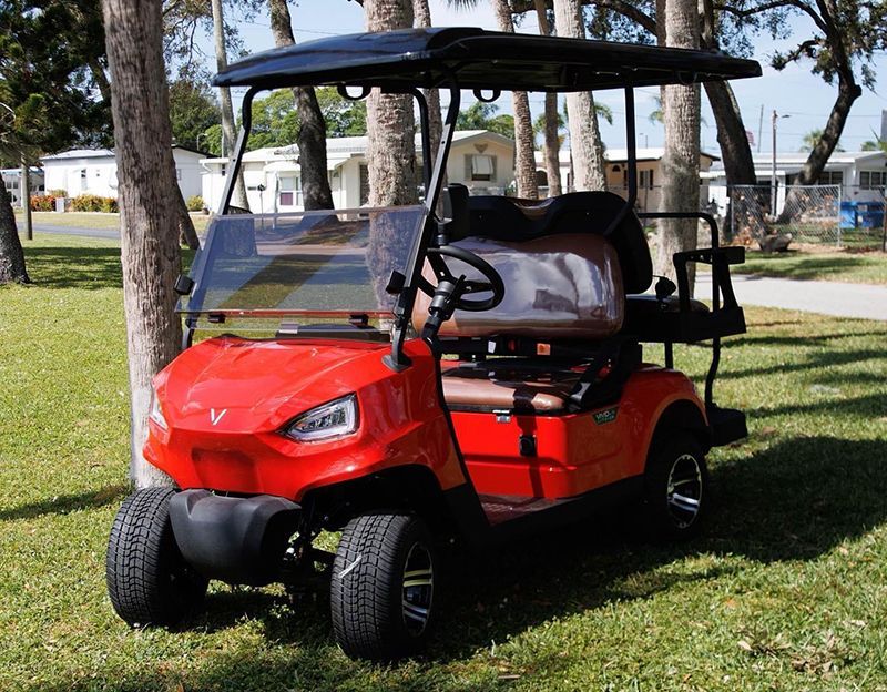 Red golf cart with black roof, parked on grass near trees.