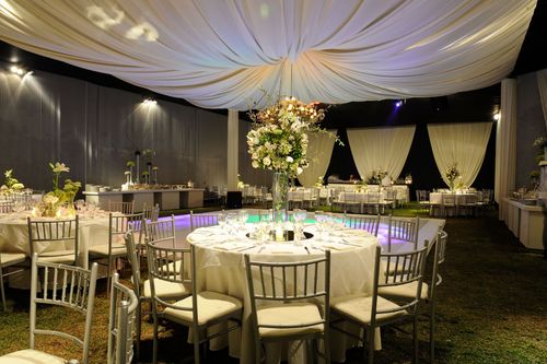 Elegant banquet hall with round tables, gold chairs, and white draped ceiling under soft lighting