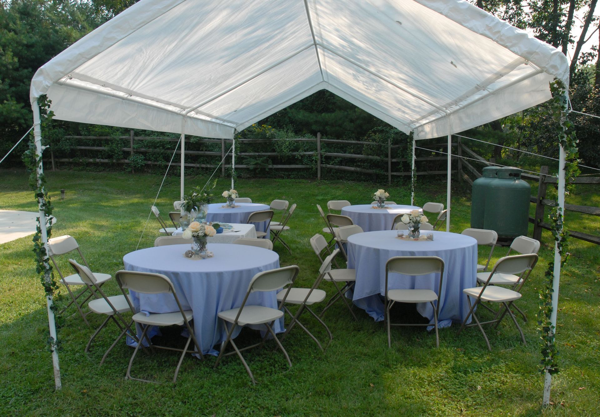 White canopy tent with round tables and chairs set up on a grassy lawn for an outdoor event