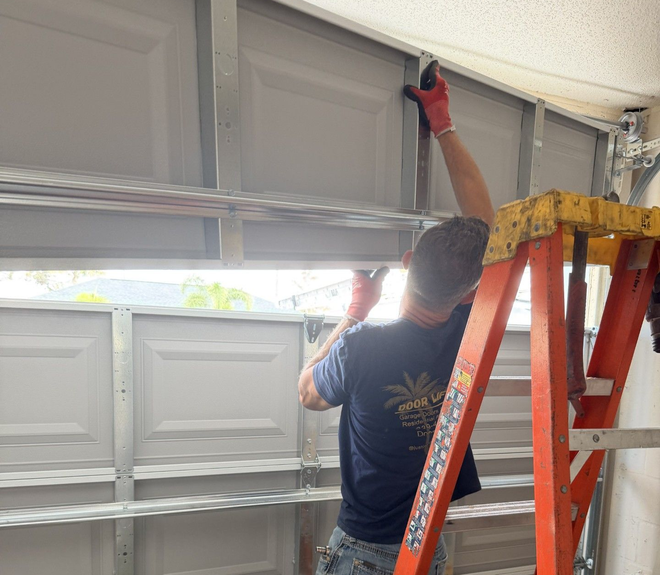 Two workers installing a garage door opener in a garage. One on a ladder, the other reaching.