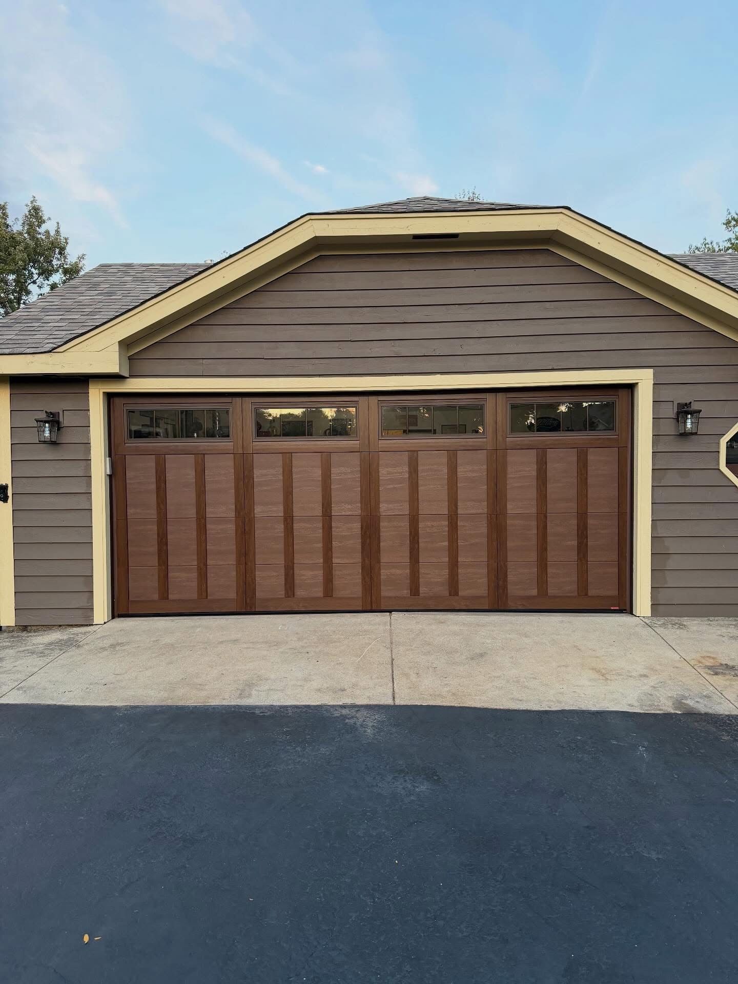 Brown garage door with windows, on a brown building with a driveway.