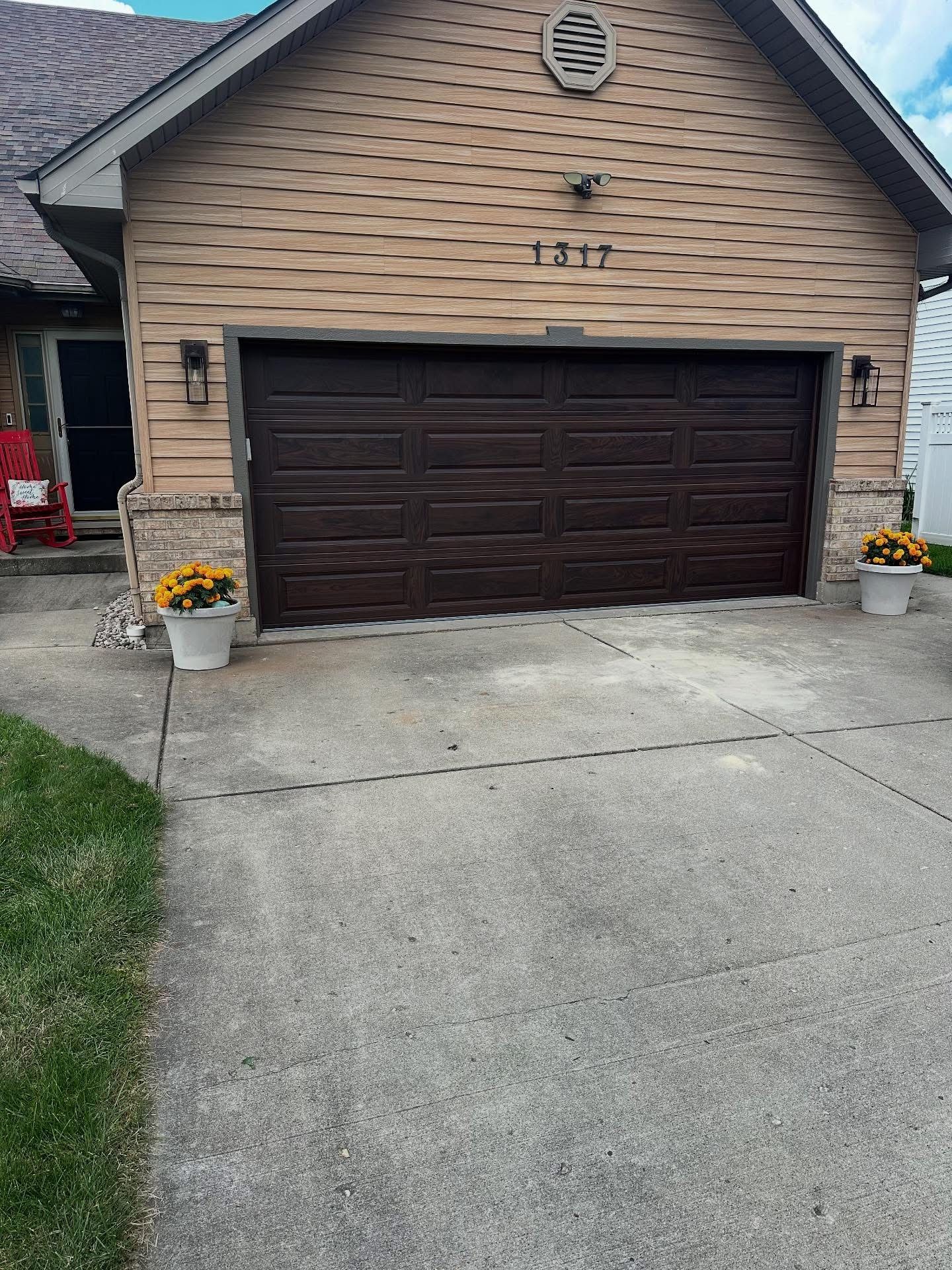 Brown garage door on a house with a concrete driveway and flower pots. The house address is 1217.