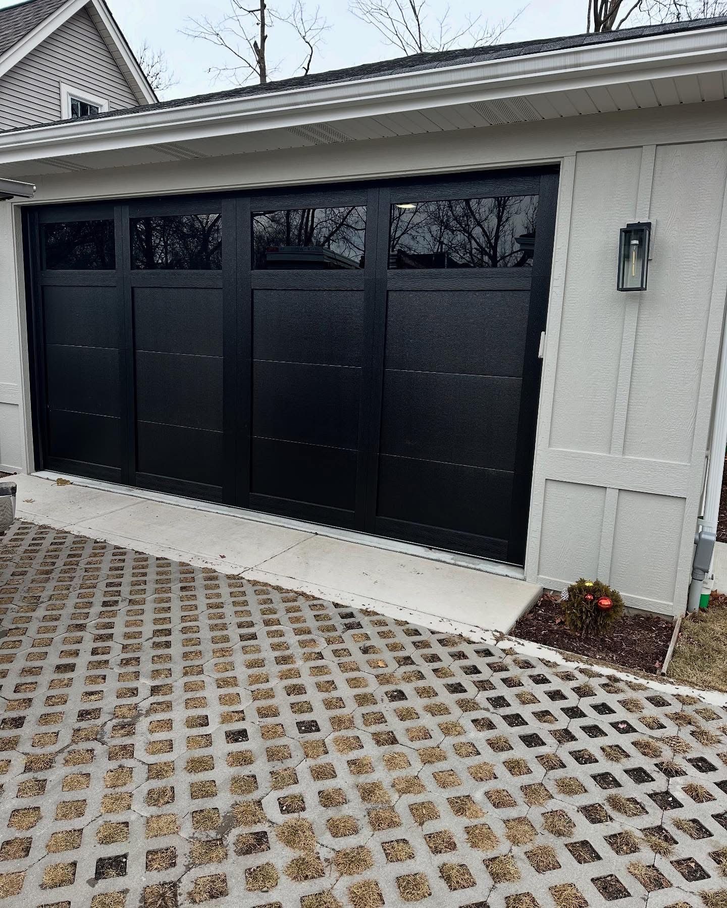 Black garage door with glass panels on a gray house; stone driveway.