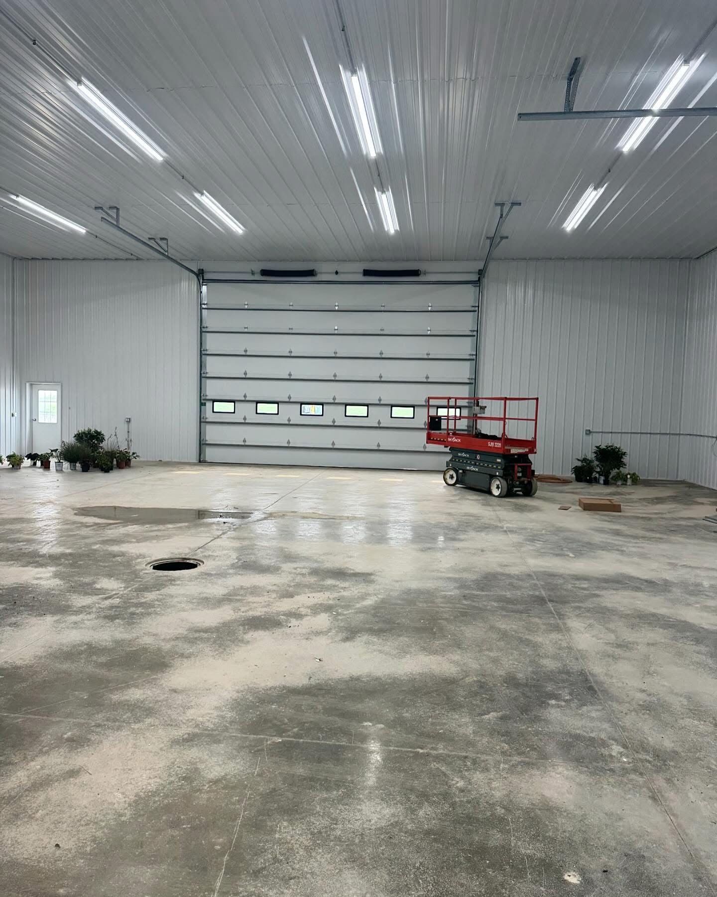 Empty industrial building interior with concrete floor, overhead door, and scissor lift.