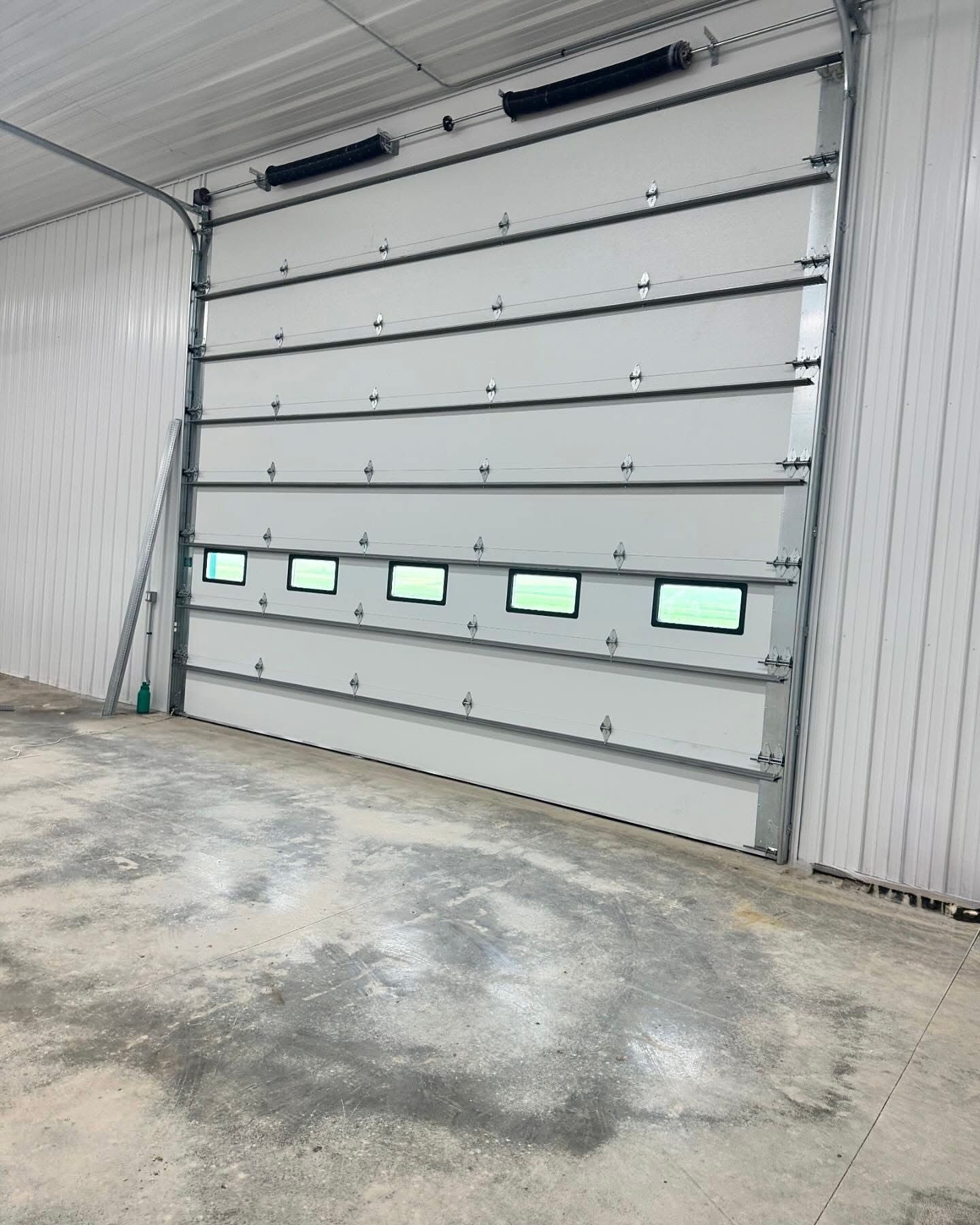 White industrial overhead door with green windows, closed, in a warehouse setting.