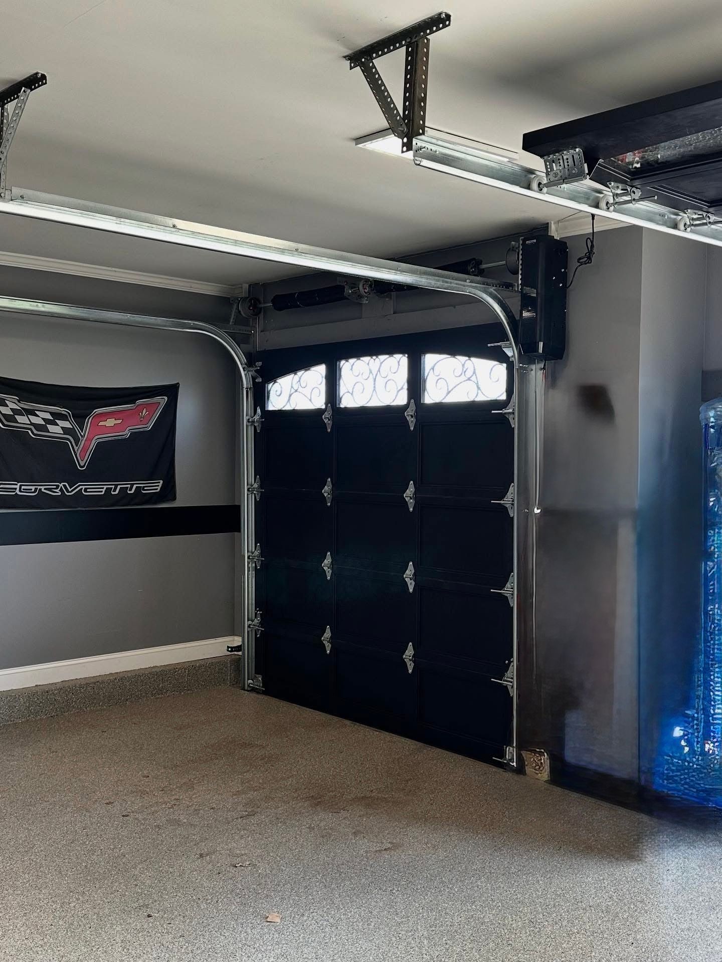 Black garage door in a gray garage with a shiny floor, partially open.