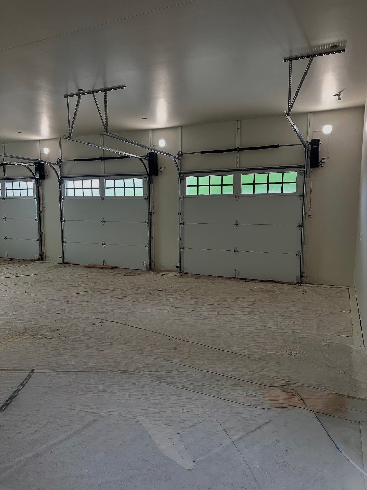 Three white garage doors with overhead openers in a concrete garage.