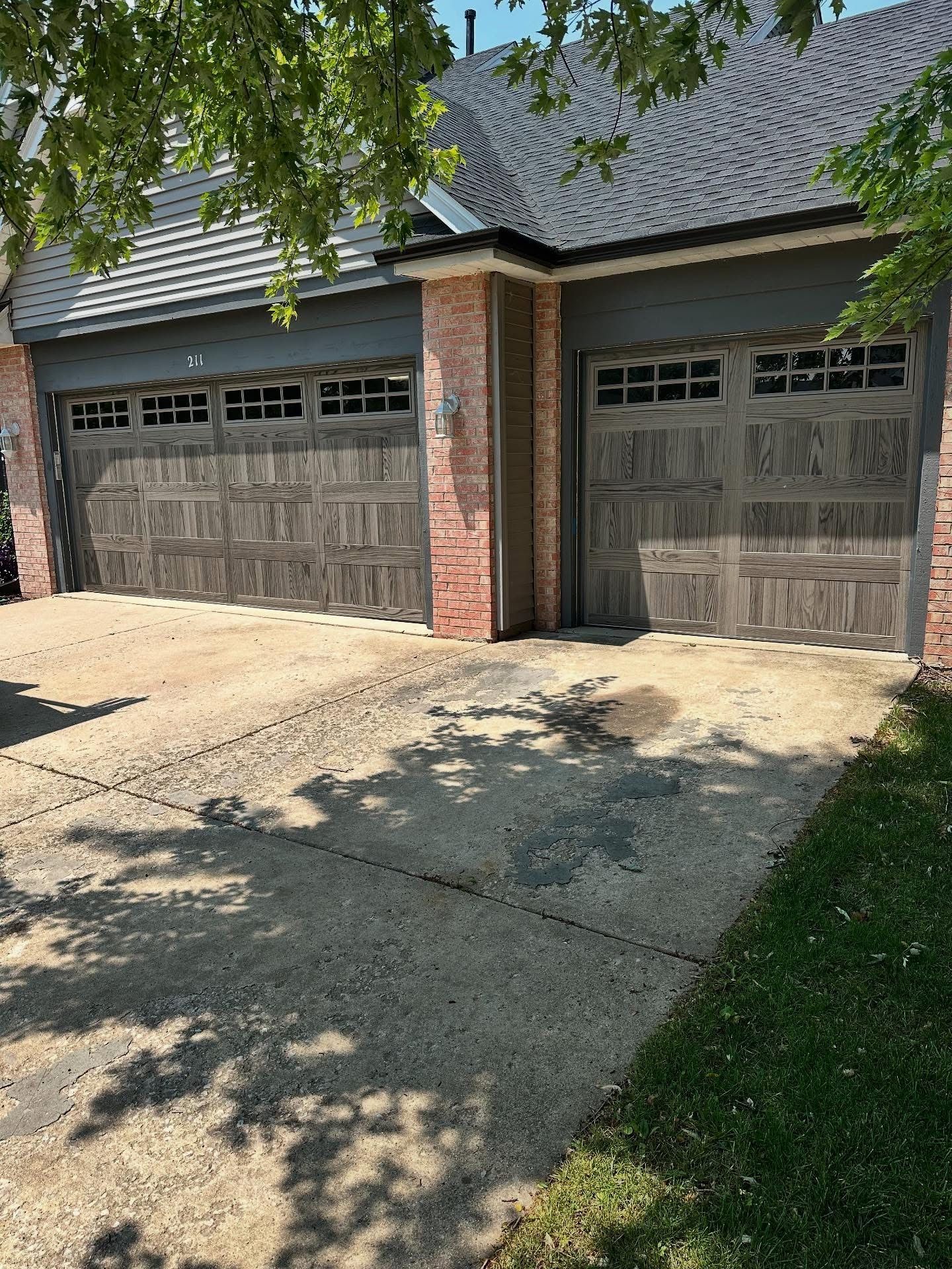 Two-car garage with brown doors and a cracked concrete driveway in front of a brick building.
