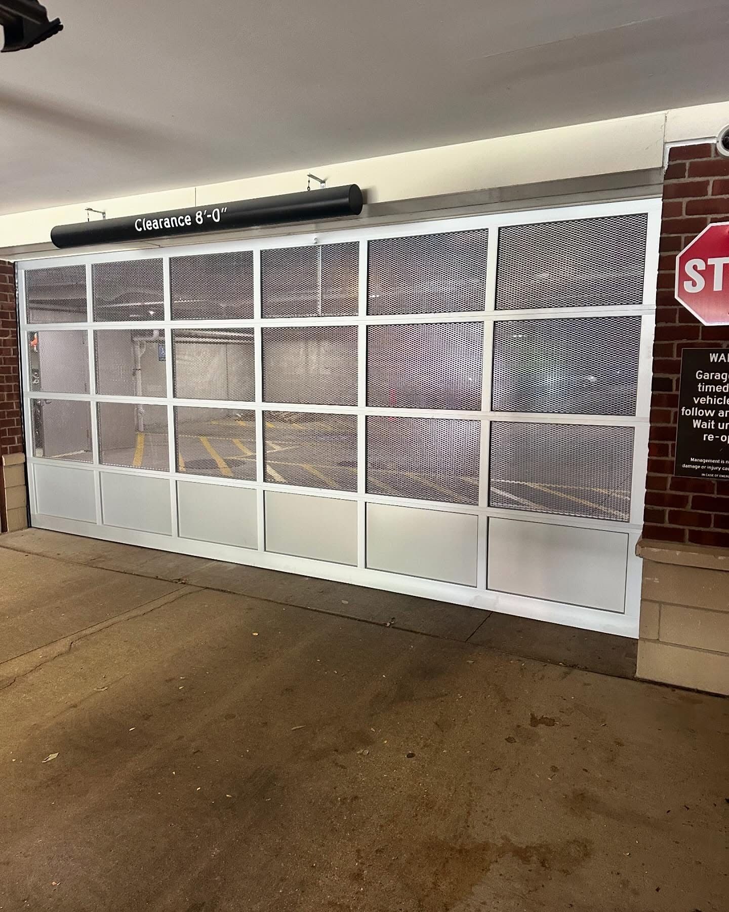 Garage door with clear panels and metal frame, brick wall, and stop sign.