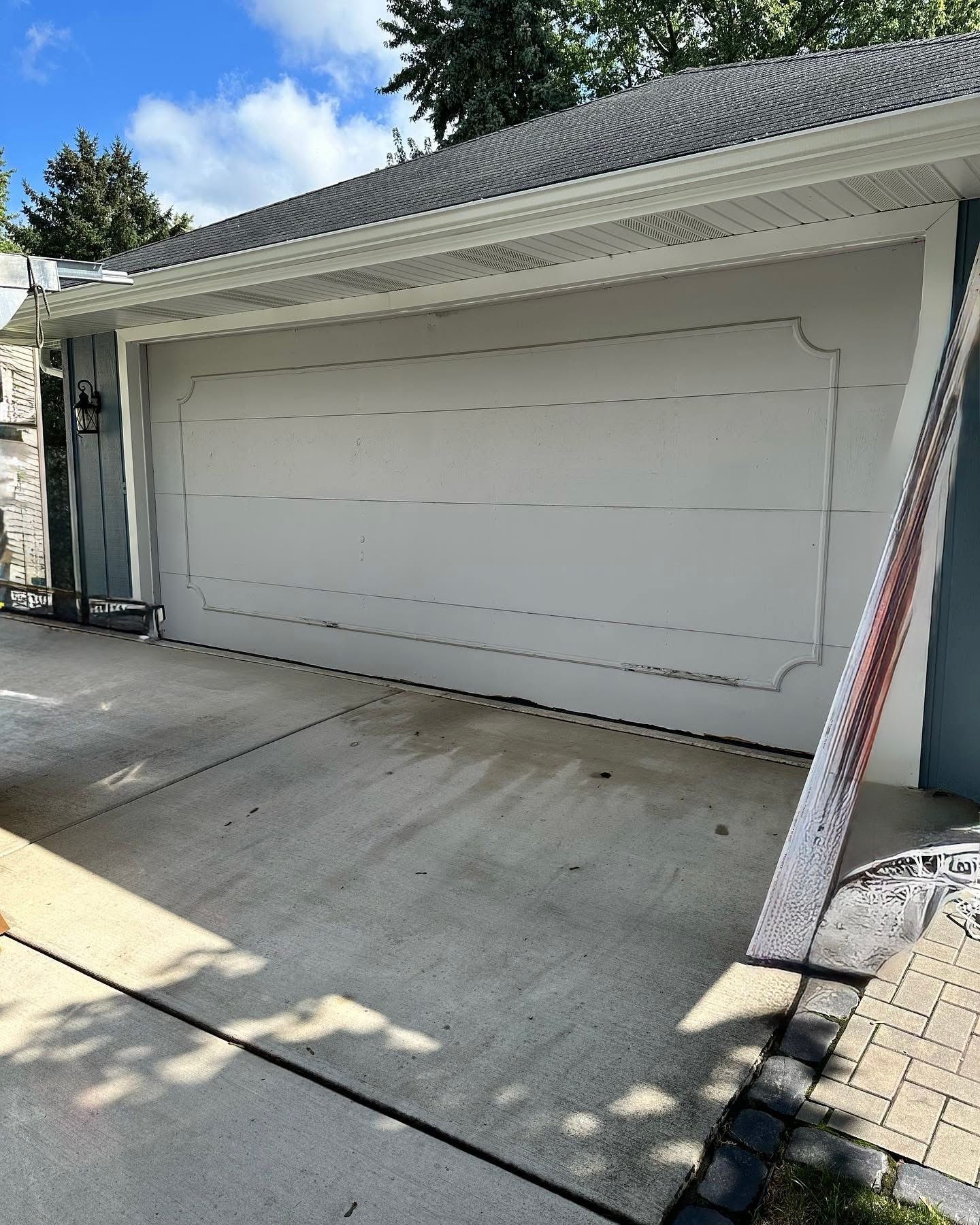 Gray garage door on a concrete driveway, next to a blue house and paved walkway.