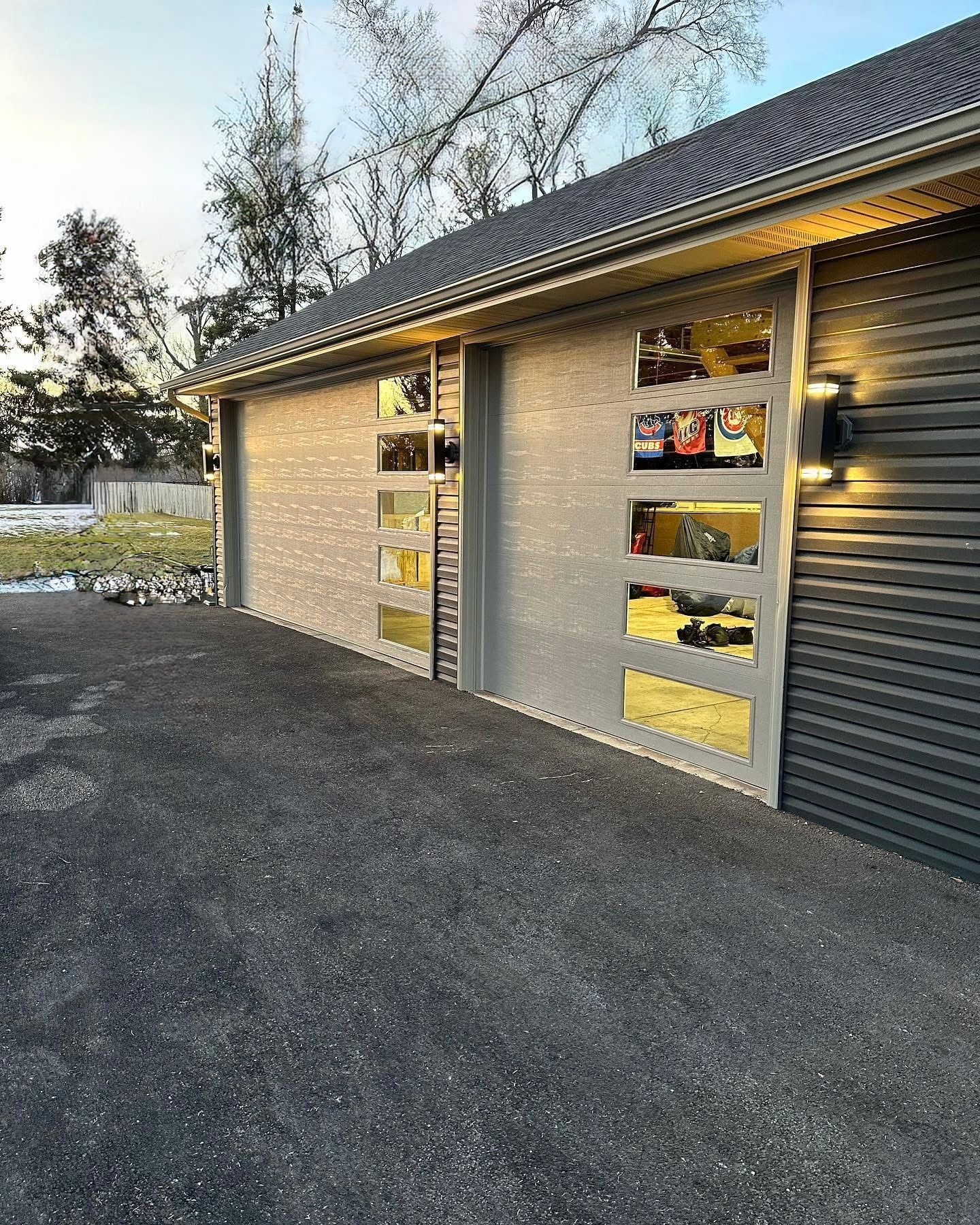 Modern garage with gray brick facade, large glass windows, and asphalt driveway.
