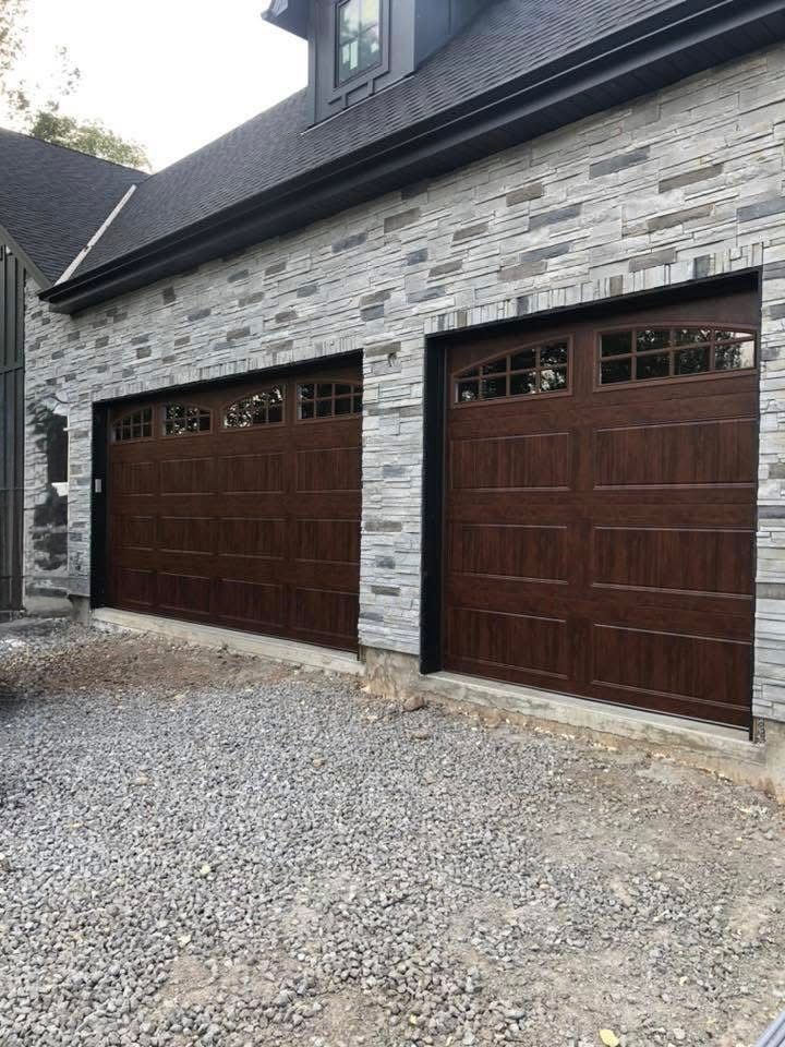 Two brown garage doors on a light gray stone building with gravel driveway.