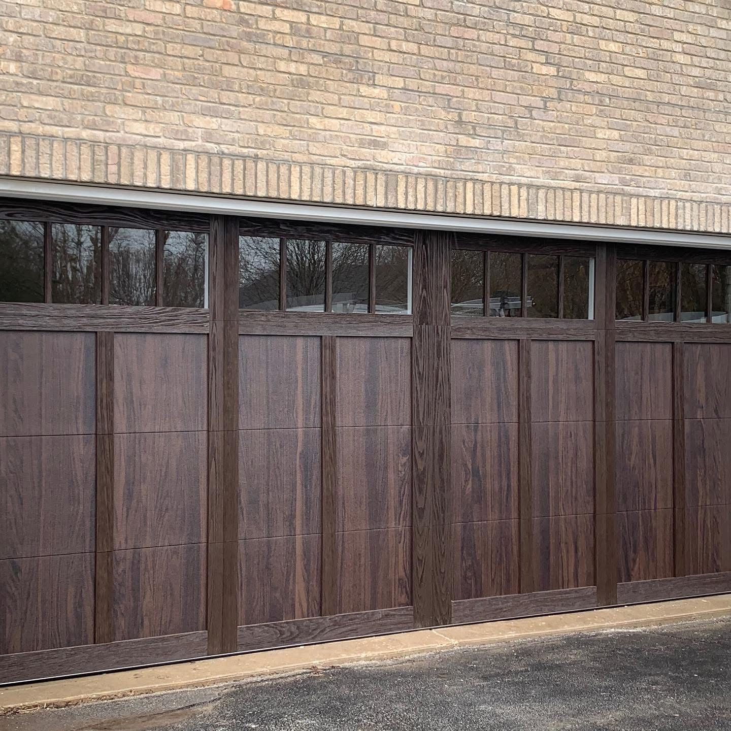 Wooden garage doors with windows, set against a brick wall.