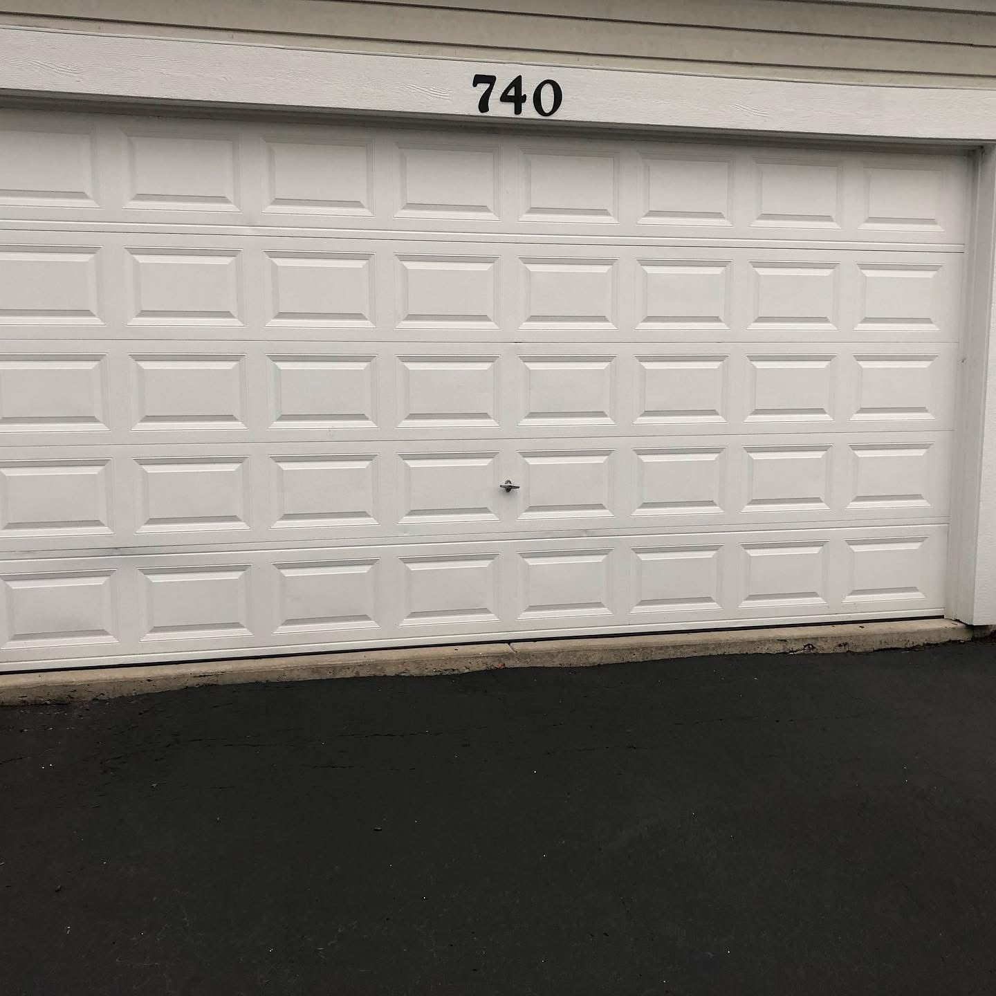 White garage door with number 740 above, set in an asphalt parking area.