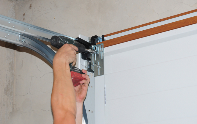 Person using a power drill to install garage door track hardware.