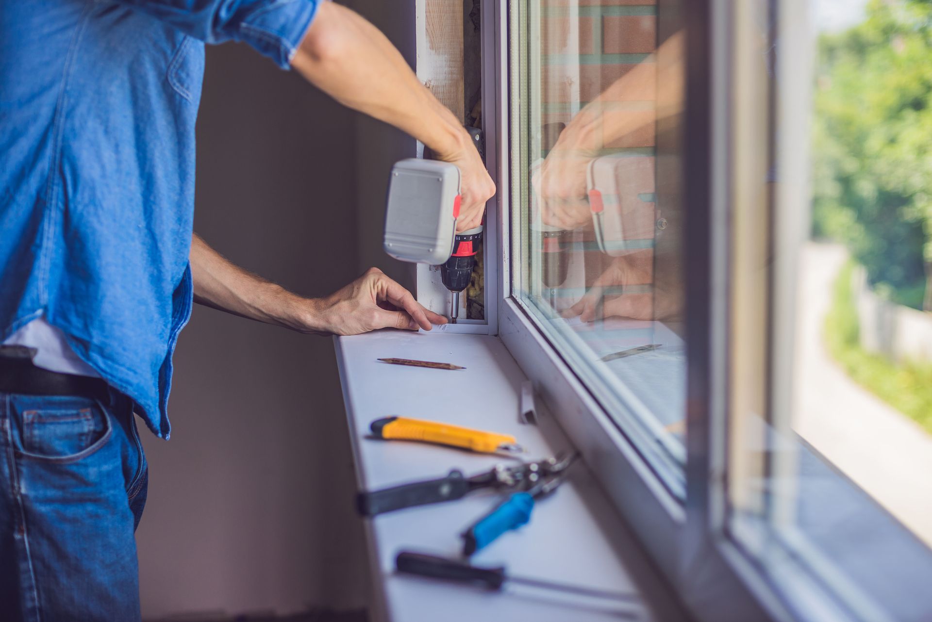 Person installing a window, using a drill. Tools visible on the windowsill.