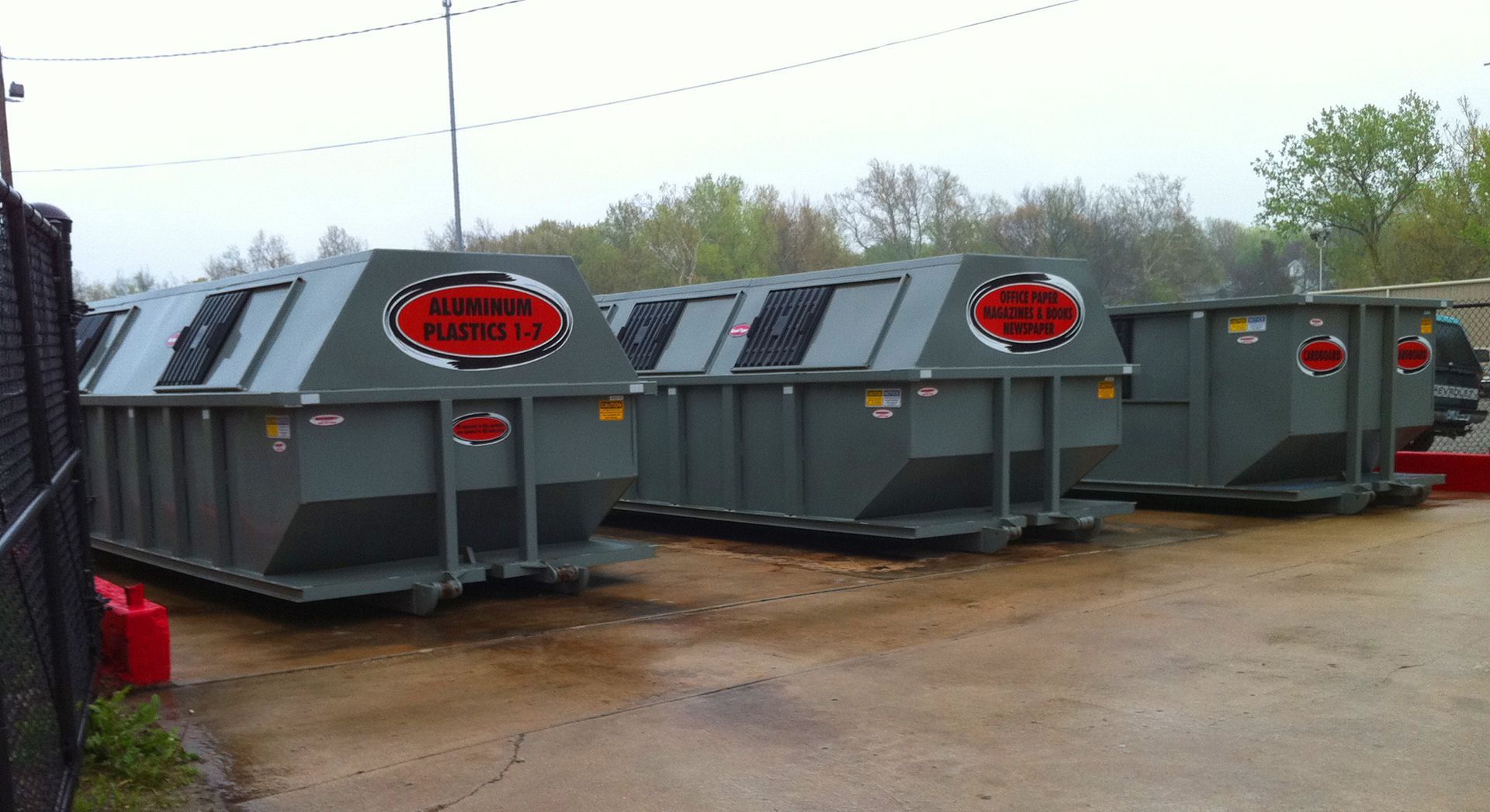 Large gray industrial dumpsters lined up outdoors on a muddy lot.