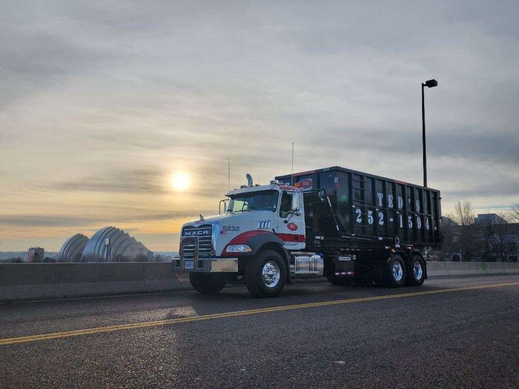White dump truck parked on a road at sunset with a bridge in the background.