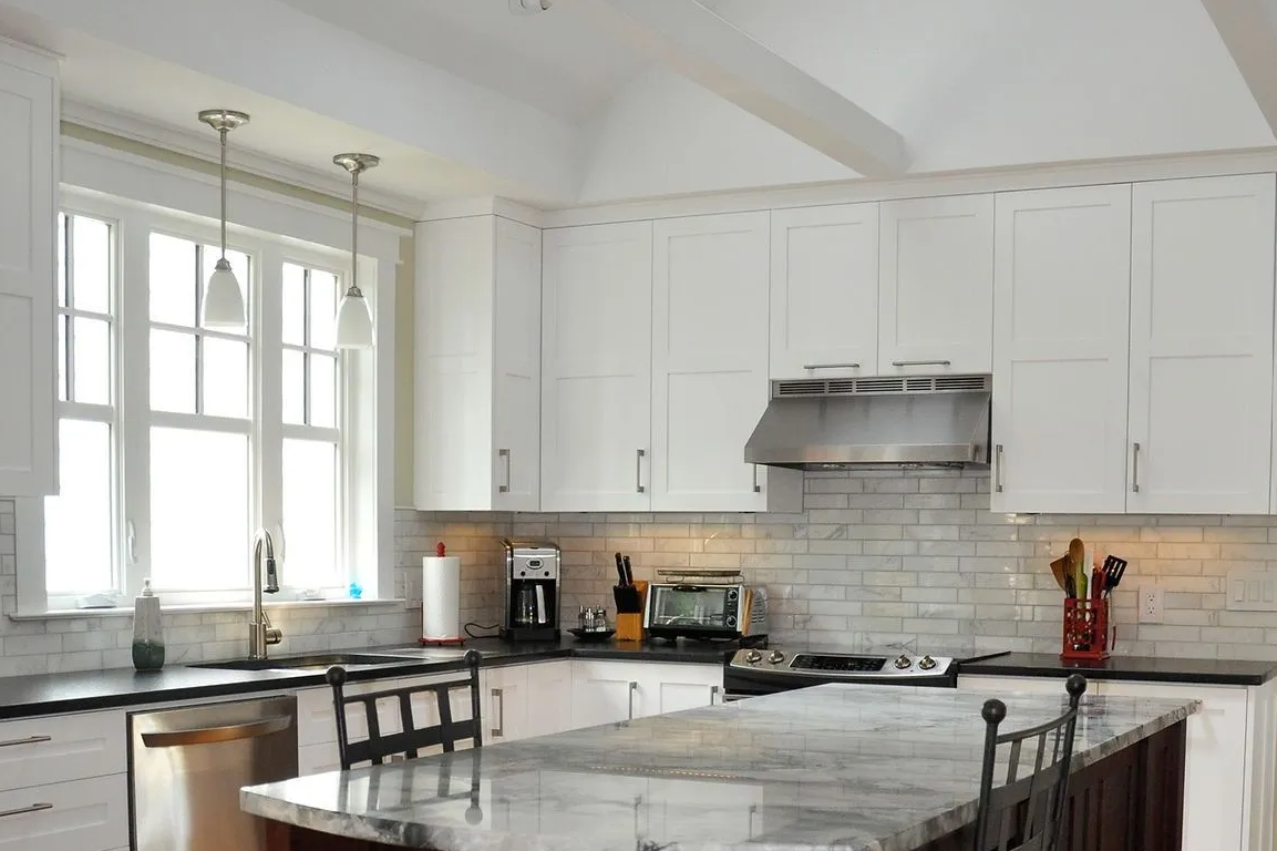 A kitchen with white cabinets , granite counter tops , stainless steel appliances and a large island.