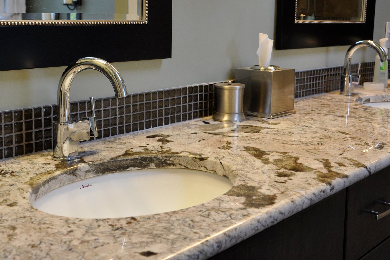 A bathroom sink with a granite counter top and two faucets.