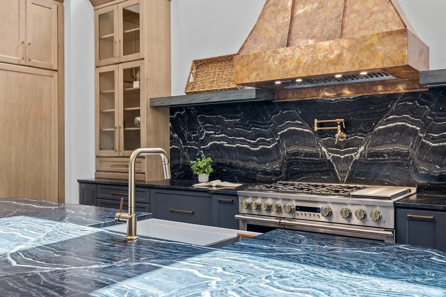 A kitchen with a stove , sink , and copper hood.