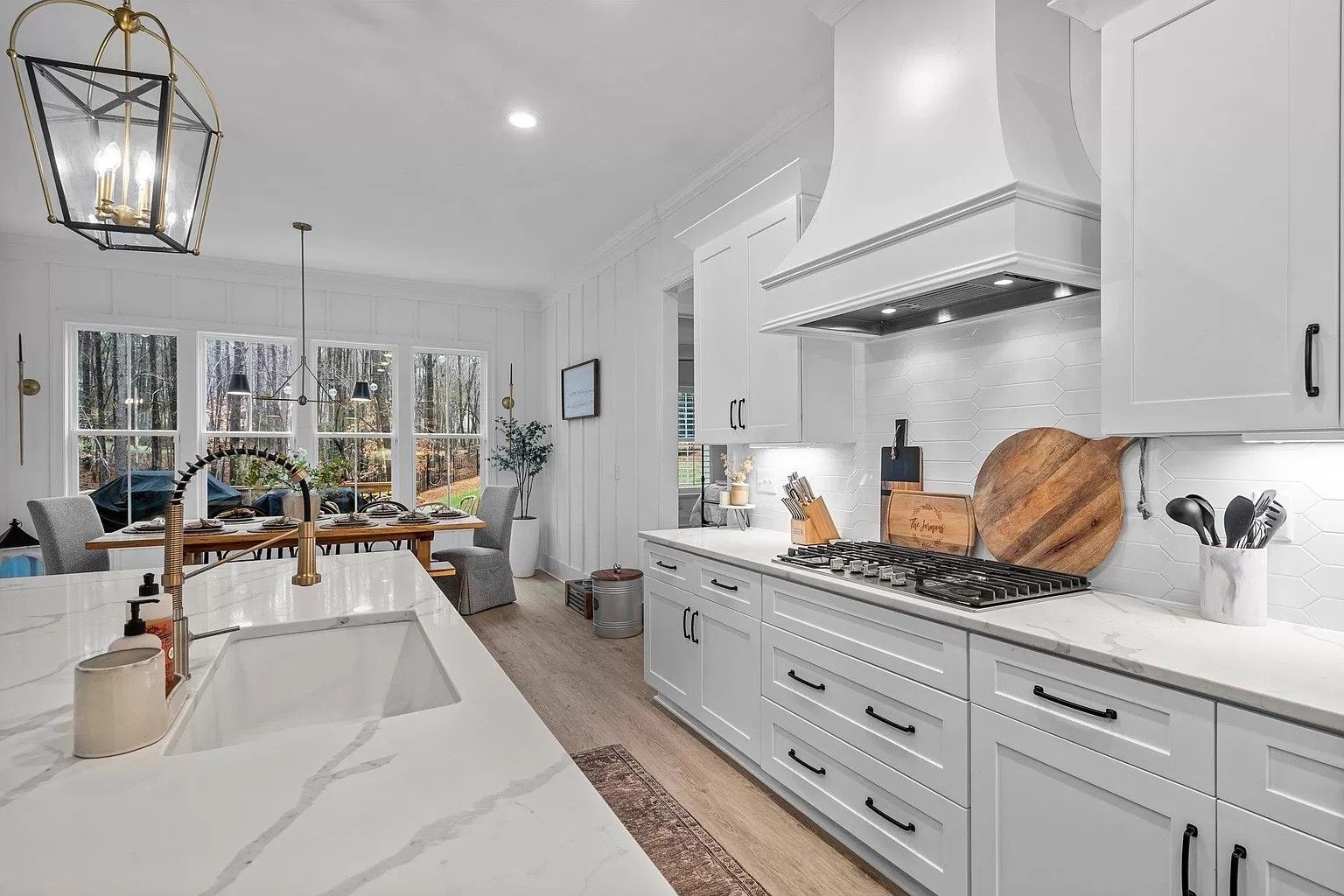 A kitchen with white cabinets , a sink , a stove , and a hood.