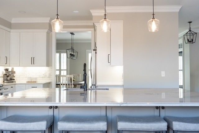 A kitchen with white cabinets and a large island with stools.