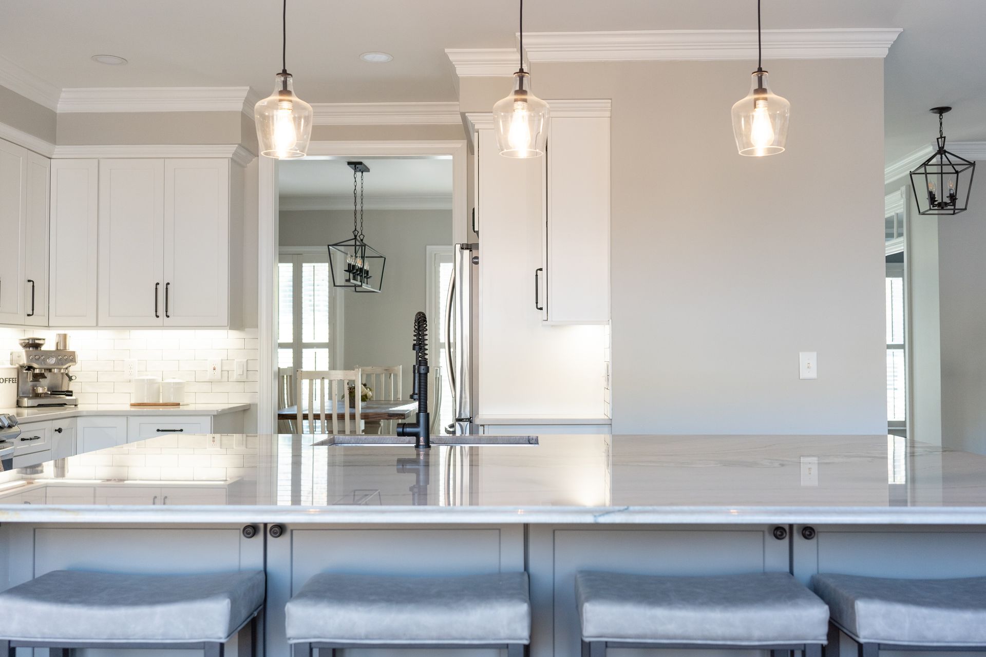 A kitchen with white cabinets and a large island with stools.
