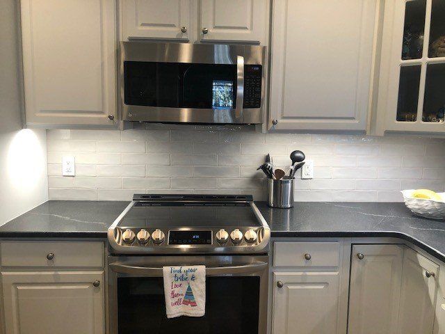 A kitchen with white cabinets , a stove , a microwave , and a towel on the counter.