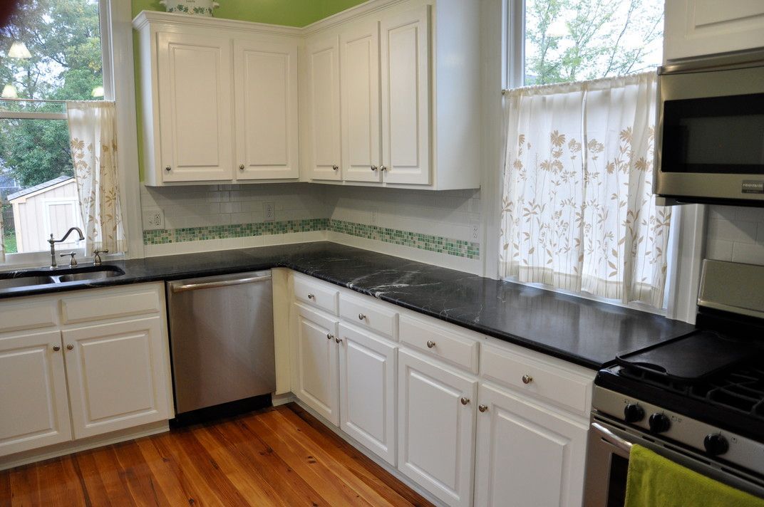 A kitchen with white cabinets , black counter tops , stainless steel appliances and a window.