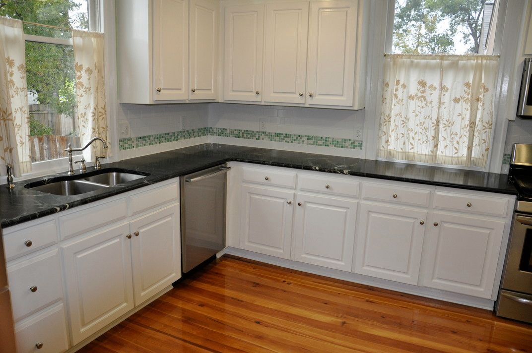 A kitchen with white cabinets and black granite counter tops.