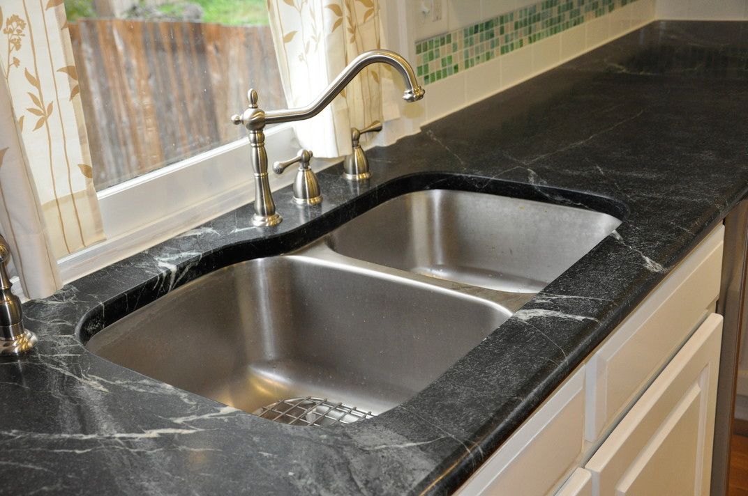 A kitchen sink with a black counter top and a window