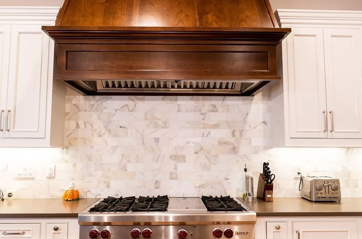 A kitchen with a stove top oven and a wooden hood above it.