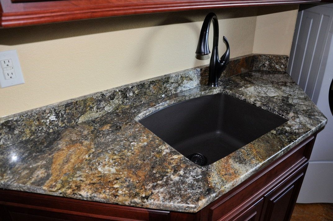 A kitchen sink with a granite counter top and a faucet