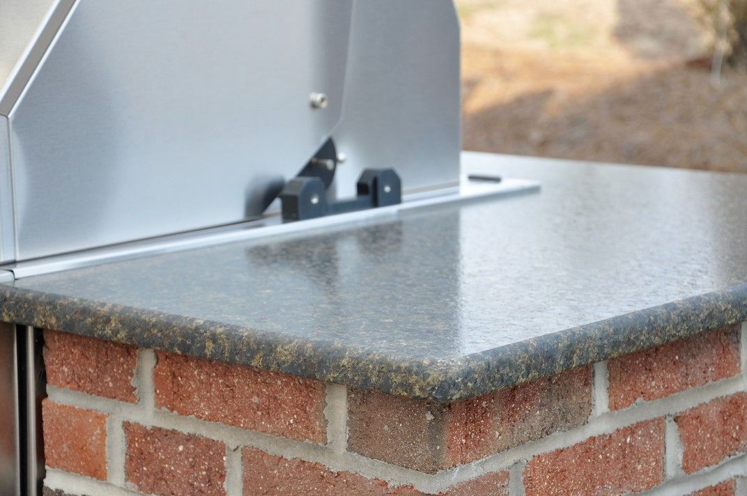 A brick wall with a stainless steel grill on top of it