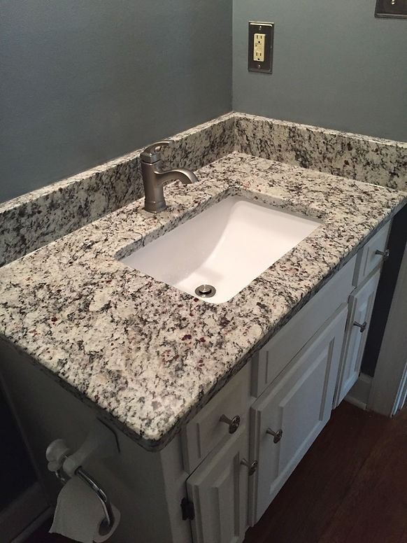 A bathroom sink with a granite counter top and white cabinets