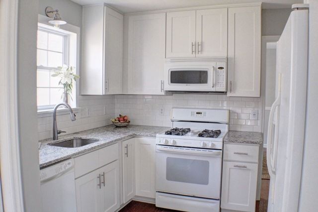 A kitchen with white cabinets , a stove , a microwave , and a sink.