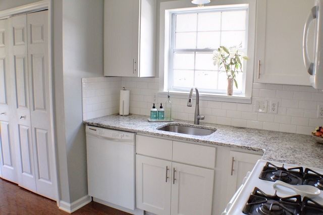A kitchen with white cabinets , a sink , a stove and a window.