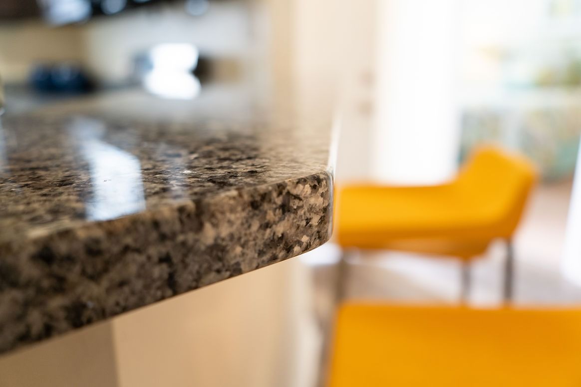 A close up of a granite counter top in a kitchen with yellow chairs in the background.