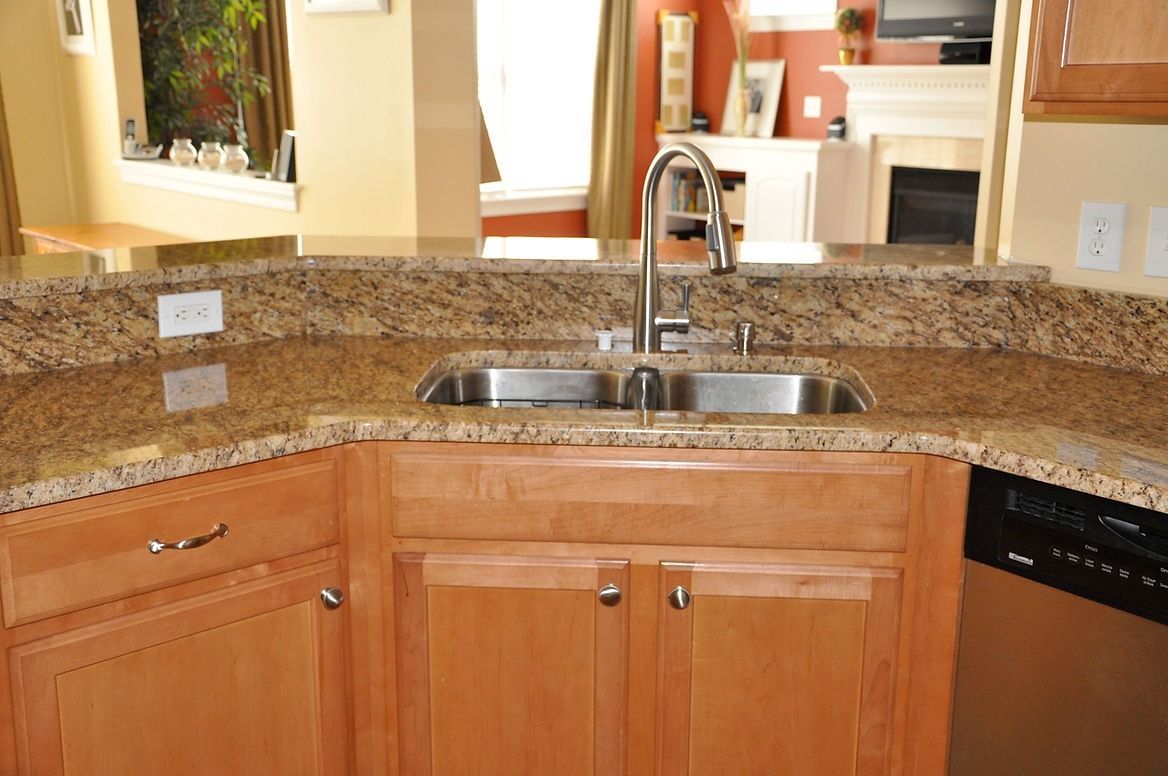 A kitchen with a sink , cabinets , granite counter tops and a dishwasher.
