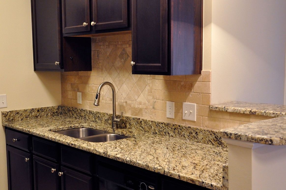 A kitchen with granite counter tops , black cabinets , a sink and a dishwasher.