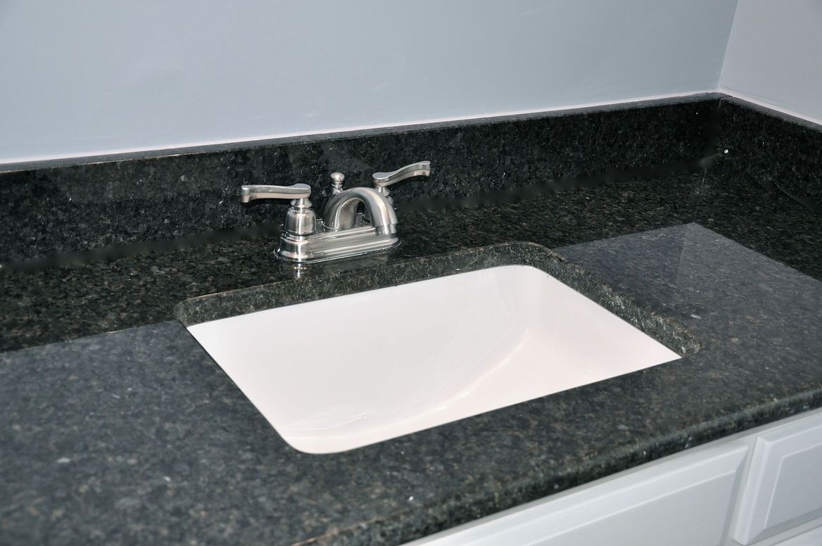 A bathroom sink with a black granite counter top and a white sink.