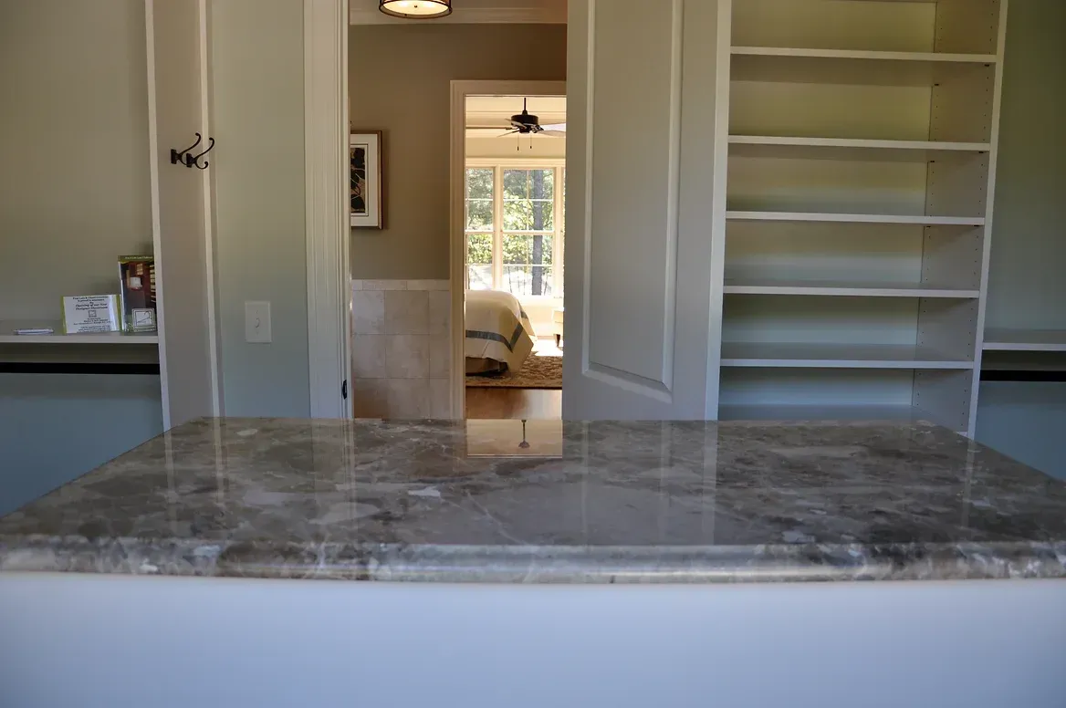 A kitchen with a marble counter top and shelves.