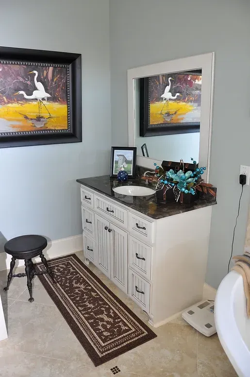 A bathroom with a sink , mirror , rug and stool.