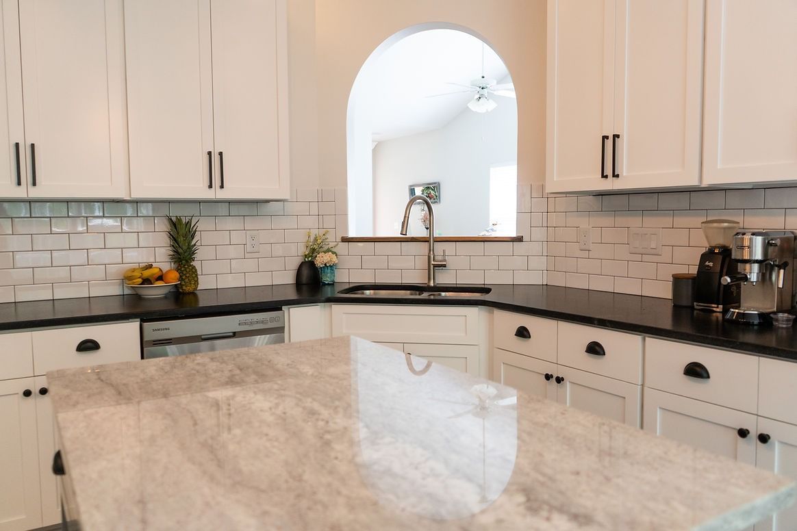 A kitchen with white cabinets , black counter tops , and a large island.