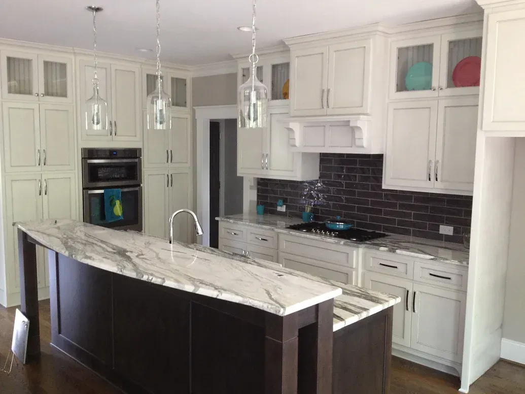 A kitchen with white cabinets , marble counter tops , and a large island.