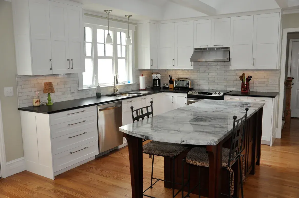 A kitchen with white cabinets , black counter tops , and a large island.
