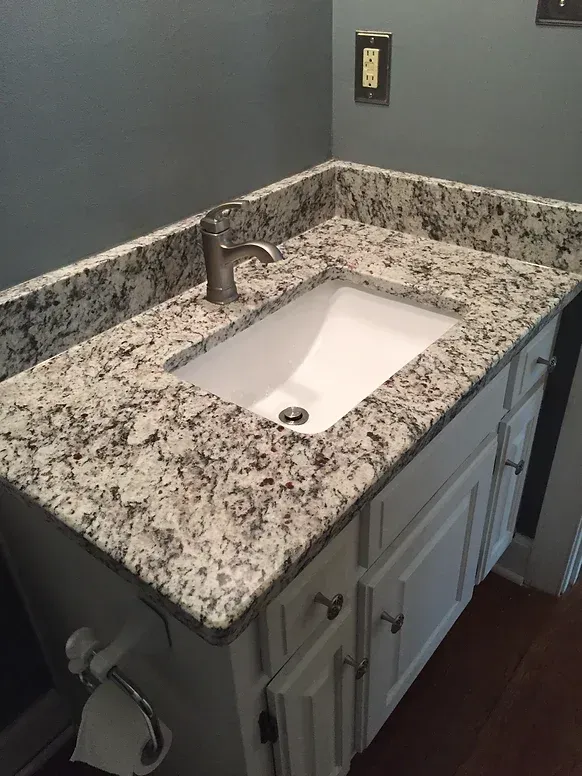 A bathroom sink with a granite counter top and white cabinets